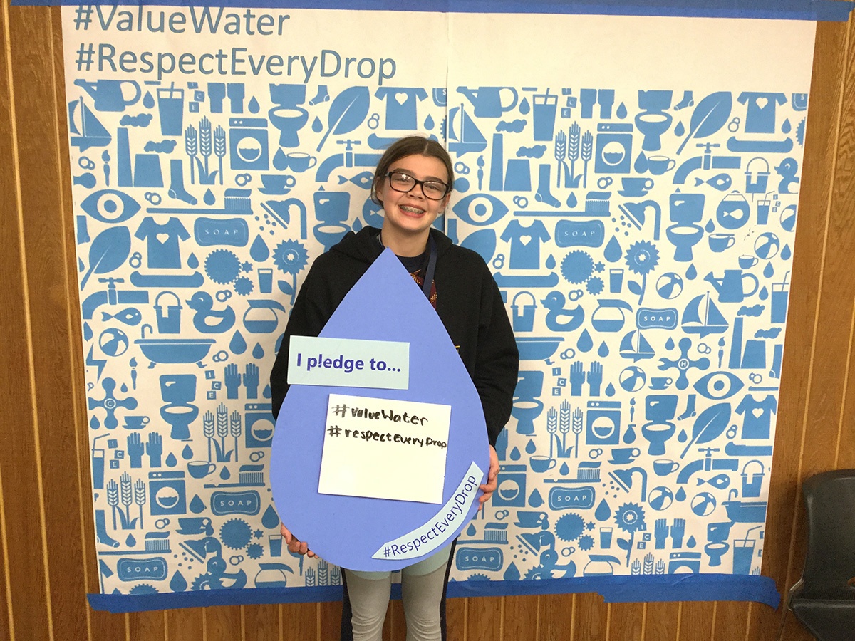 A young girl holding a sign that says "I pledge to value water and respect every drop."